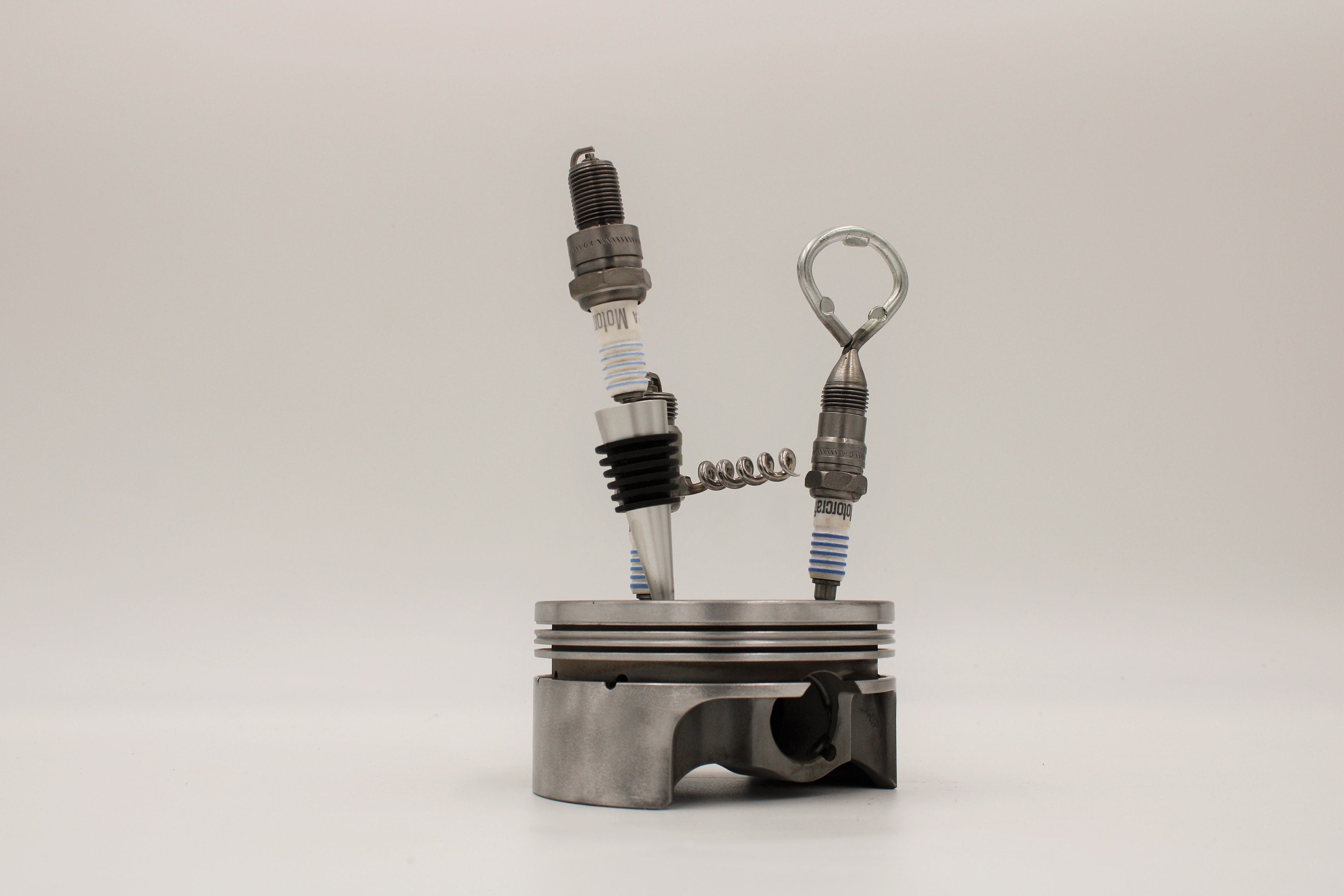 Spark plug bar set including a wine stopper, corkscrew and bottle opener, all made from car spark plugs and in a car piston holder.