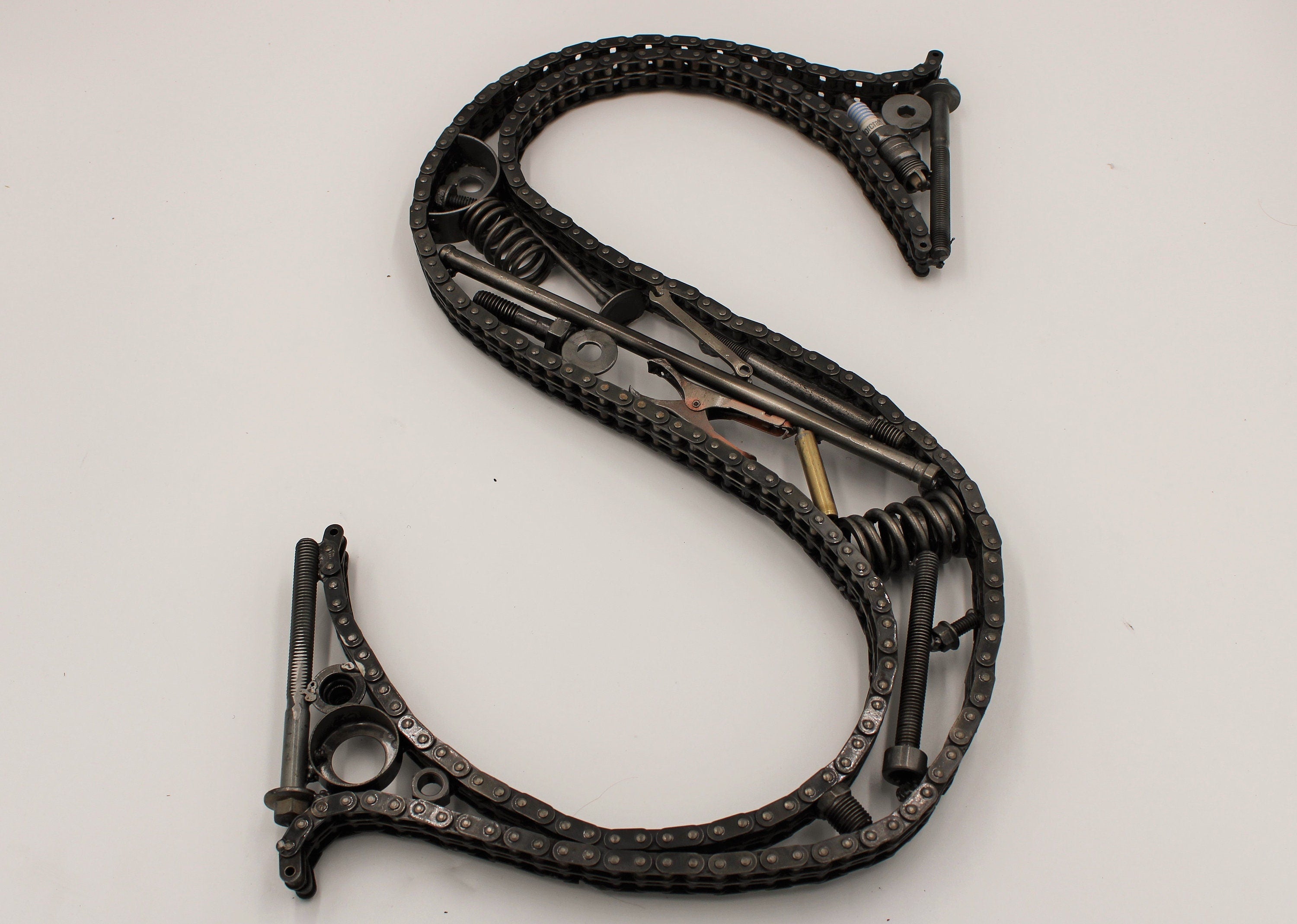 A letter S made out of real car parts, outlined with a car's timing chain.
