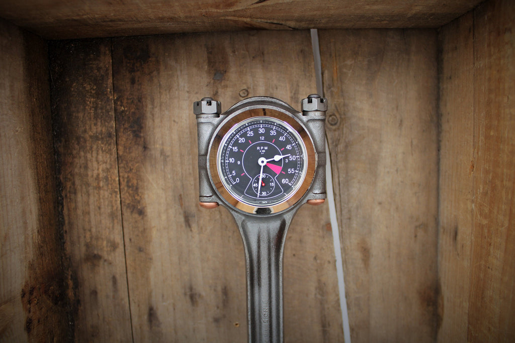 A piston clock made out of a Jaguar E-type XKE car piston, finished in gunmetal gray with a gold clock ring.