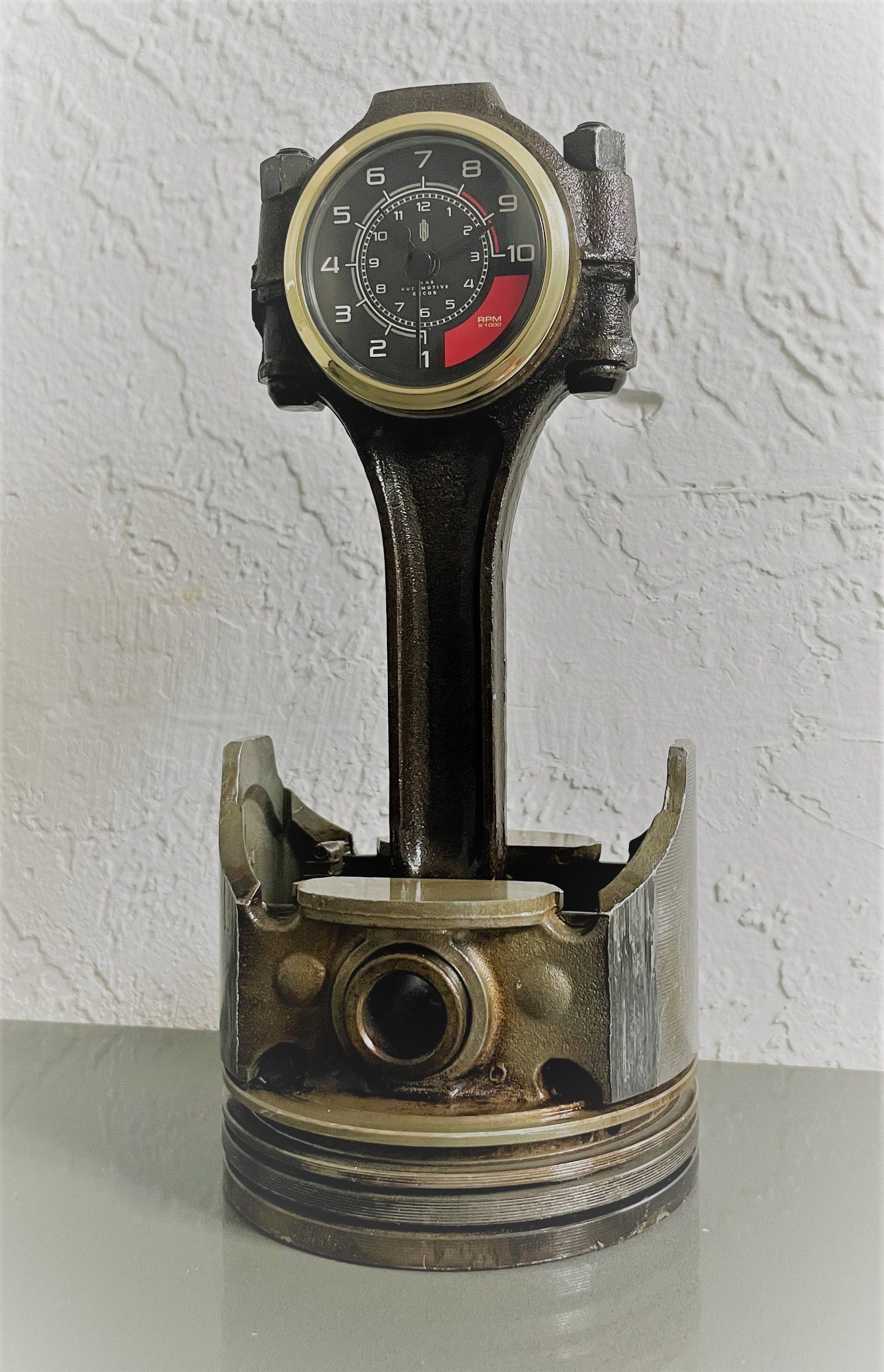 A car piston clock in a patina finish with a gold clock ring and custom black and red RPM clock face.