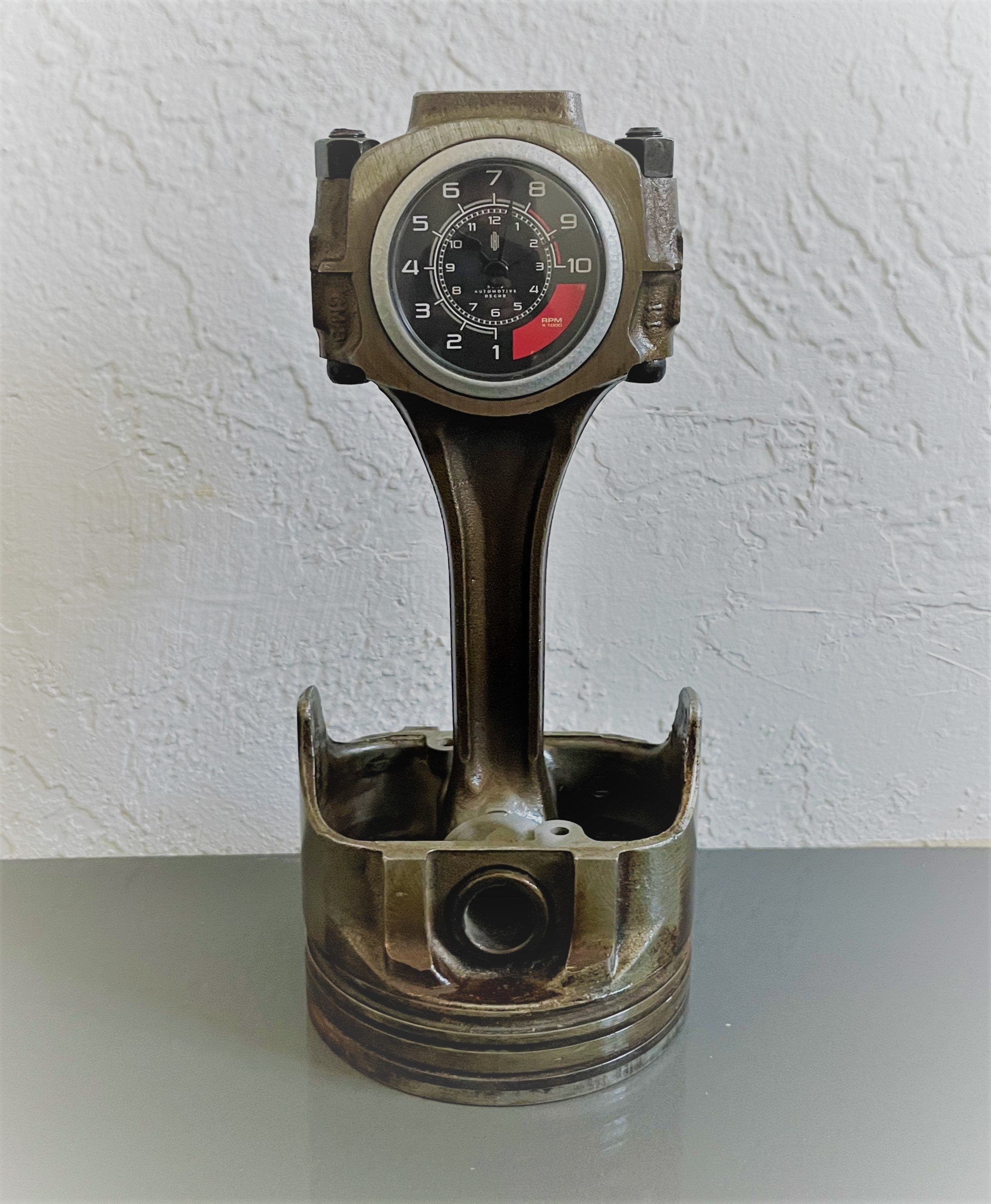 A car piston clock in a patina finish with a silver clock ring and a custom black and red RPM clock face.