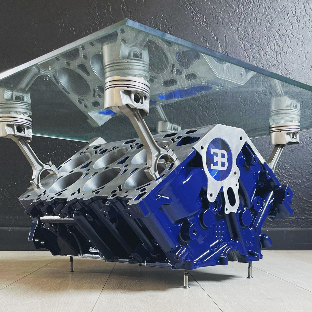 Engine block coffee table painted blue, with its square glass top being held up by car engine pistons.